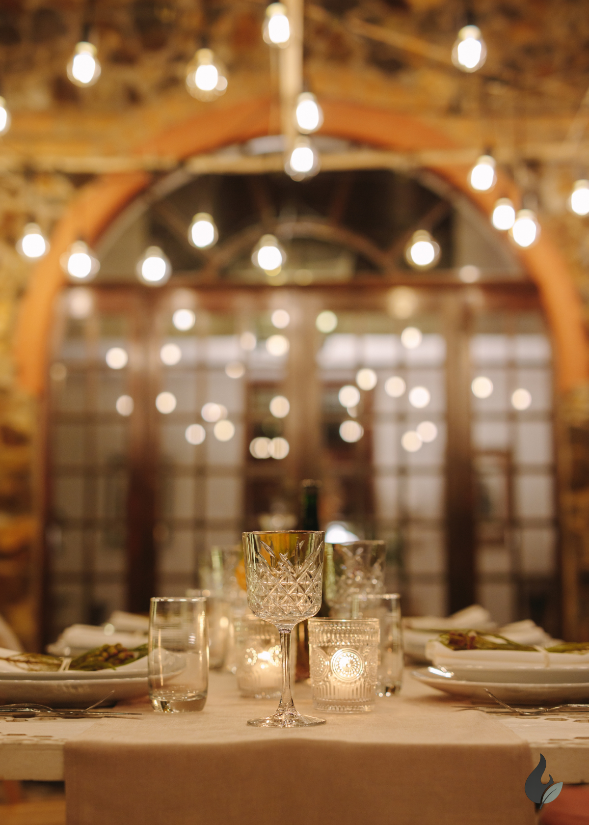 Dining table set with glasses and candles under string lights in a rustic setting